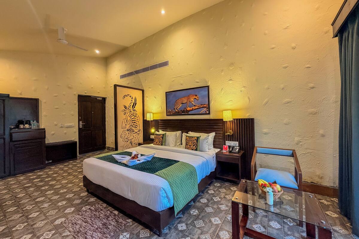 A hotel room with a large bed, a desk, a chair, a TV, and a tiger artwork on the wall.