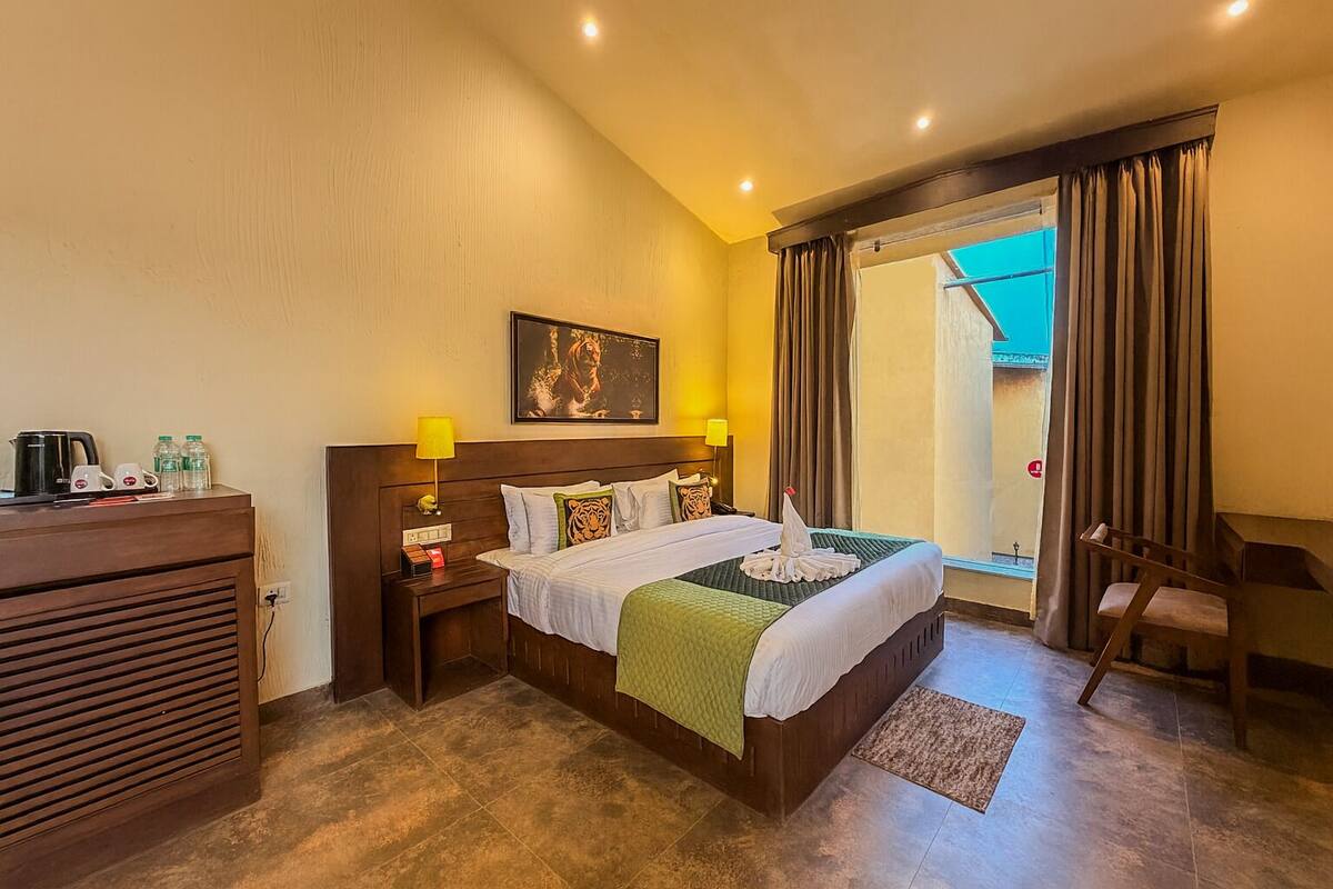 A hotel room with a bed, bedside table, lamp, and a view of the outside.