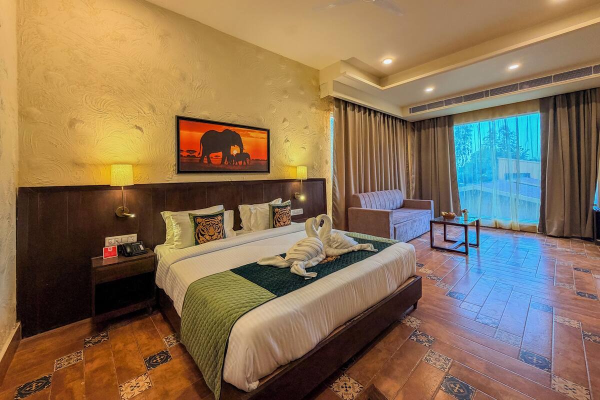 A hotel room with a large bed, a sofa, a desk, and a view of the outdoors.