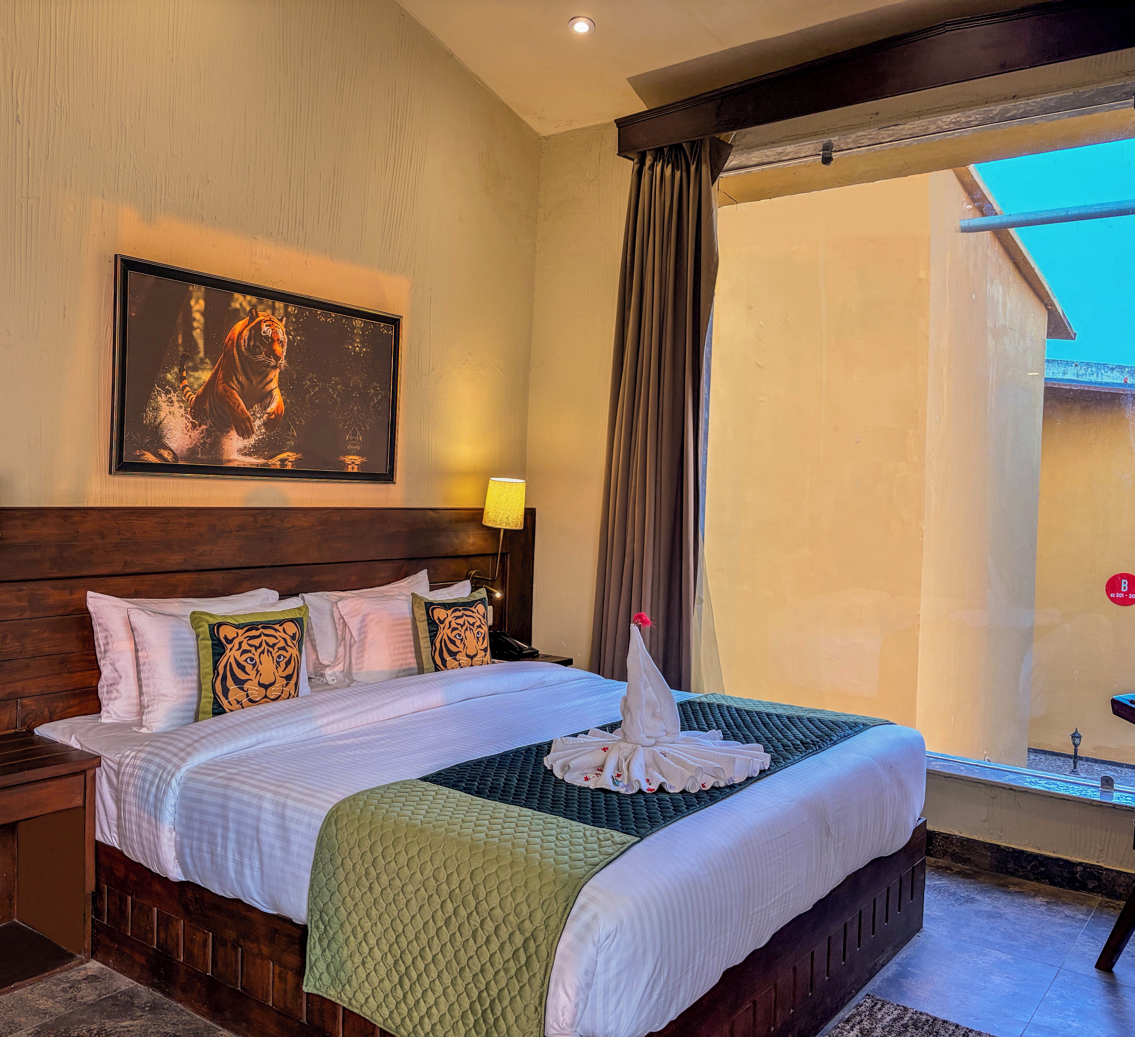 Une chambre d’hôtel avec un grand lit, une tête de lit, un tableau représentant un tigre, une fenêtre avec des rideaux et une table de chevet avec une lampe.