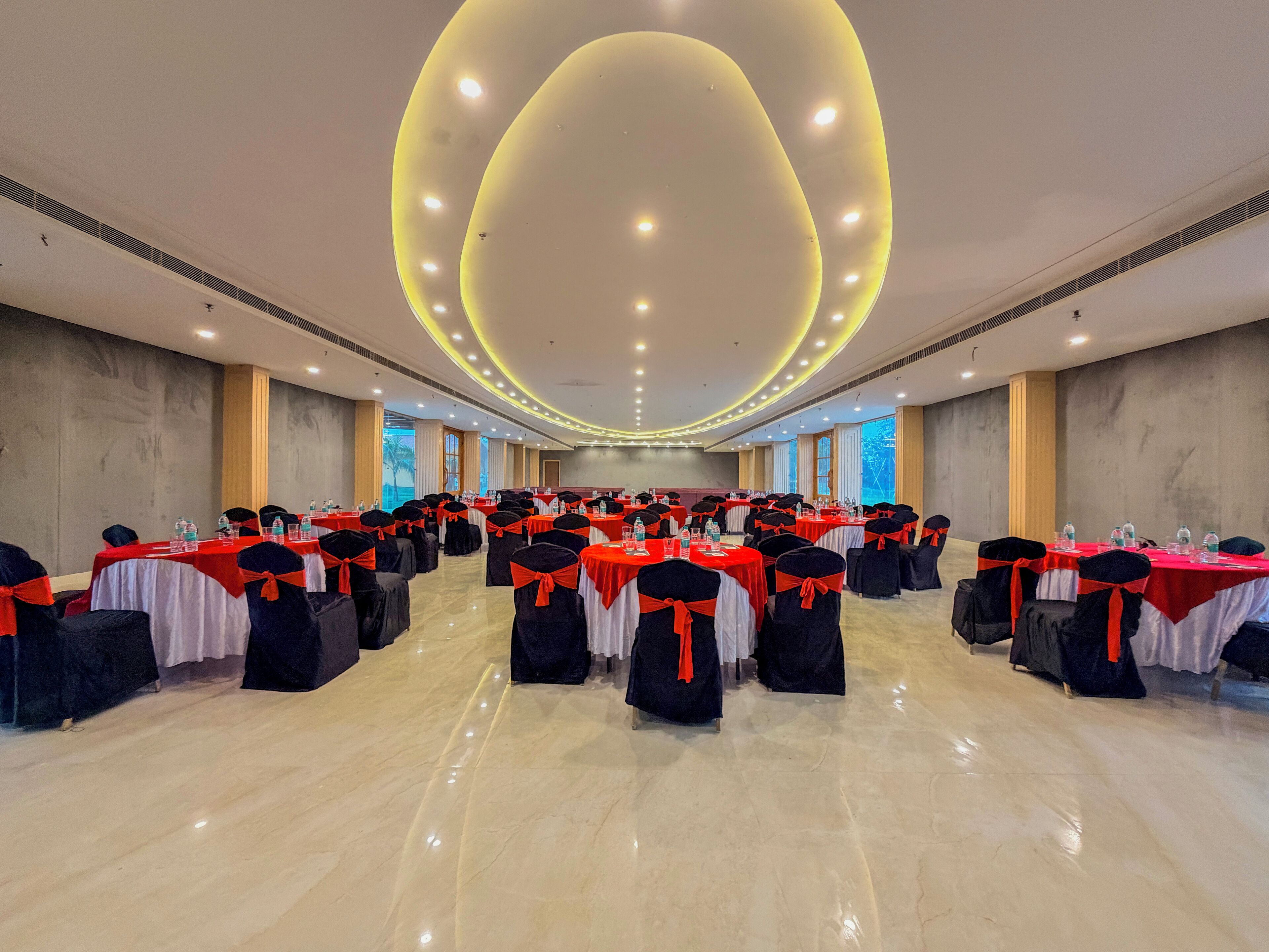 Un'ampia sala conferenze con file di tavoli, sedie nere decorate con nastri rossi e un moderno design del soffitto.