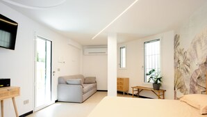 A modern bedroom with a bed, a sofa, a TV, and a window with a plant. - SECRET SUITE VARIGOTTI (Varigotti)