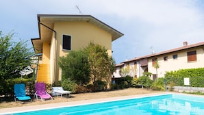 Une maison à deux étages avec une piscine, un espace salon extérieur et un jardin.