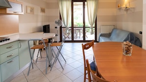 Une cuisine compacte avec un coin repas, un ventilateur et une vue à travers la porte vitrée.
