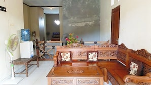 A traditional wooden sofa set with intricate carvings, a matching coffee table, and a fan. - Lishafa Homestay (Karimun Jawa)