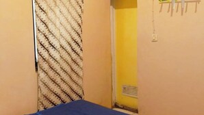 A room with a bed covered by a blue blanket, a patterned curtain, and a yellow wall. - Lishafa Homestay (Karimun Jawa)