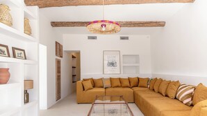 A modern living room with a large sectional sofa, a glass coffee table, and a hanging woven light fixture. - Maison Paula - In the heart of the village & heated pool (Oppède)