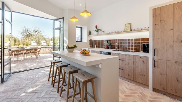 A modern kitchen with a large island, wooden stools, and a view of the outdoor patio area. - Maison Paula - In the heart of the village & heated pool (Oppède)