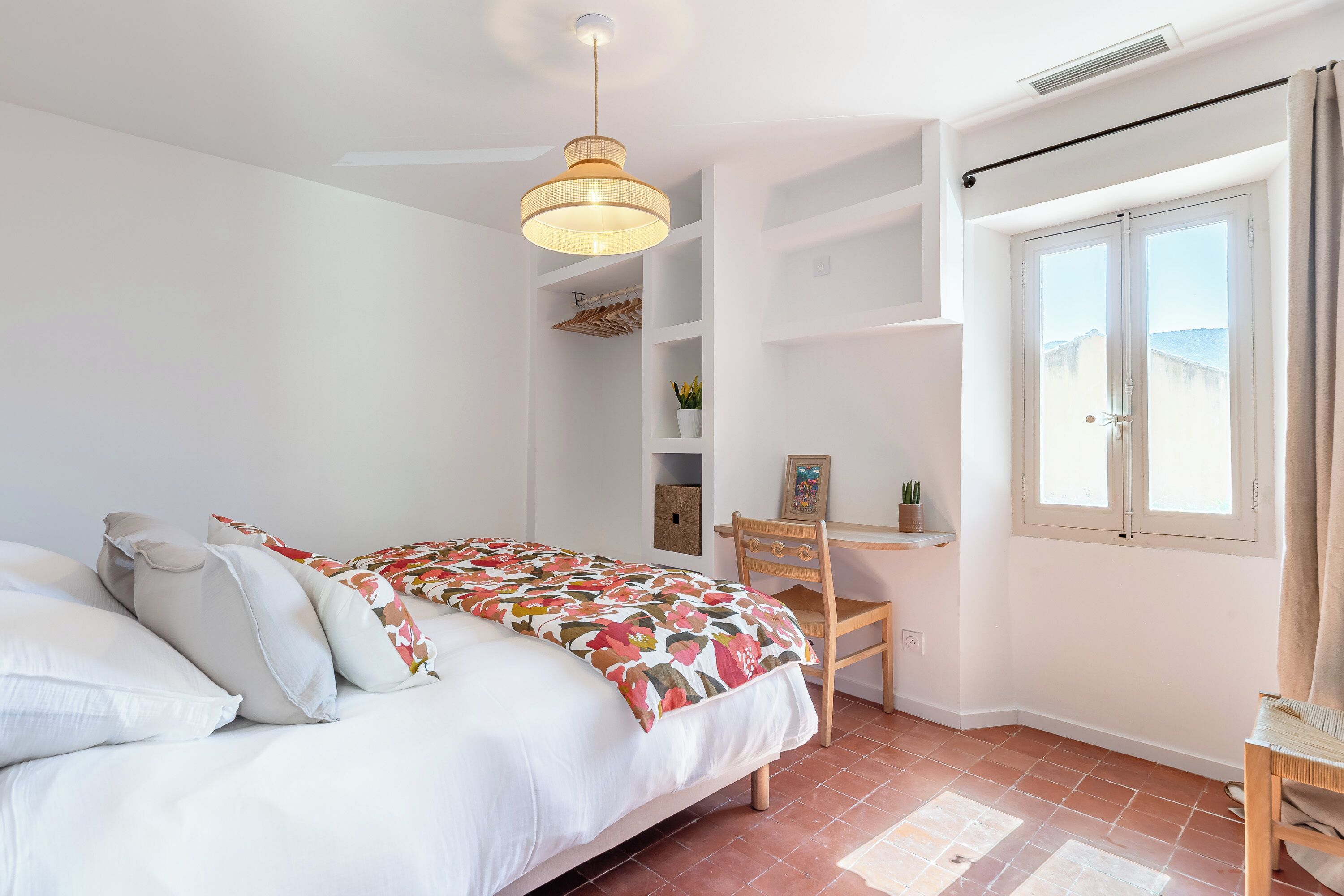 Een slaapkamer met een bed, een bureau, een stoel, een raam en een plafondventilator.