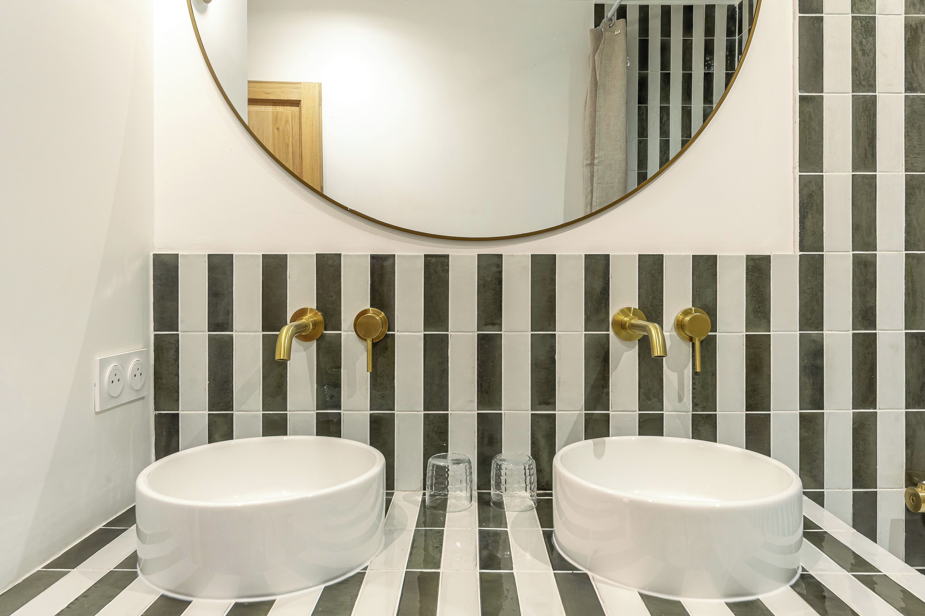 A bathroom with two white sinks, a round mirror, and a tiled backsplash.