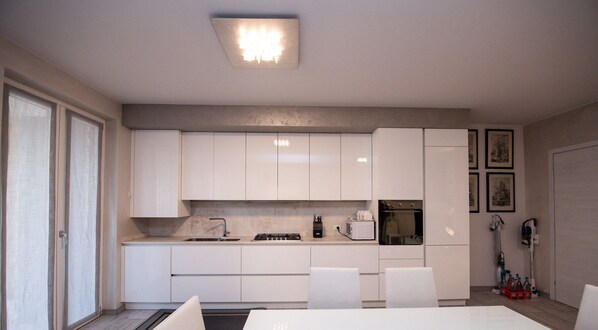 A modern kitchen with white cabinets, a dining table, and chairs. There is a microwave, a kettle, and a sink. - Oasi Bell Incanto in Calvagese Della Riviera (Calvagese della Riviera)