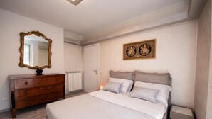 Een slaapkamer met een bed, een dressoir, een spiegel, een radiator en decoratieve wandkunst.
