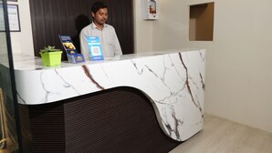 A reception desk with a marble top, a green plant, and informational brochures. - Hotel Paradise Premier (Danapur)