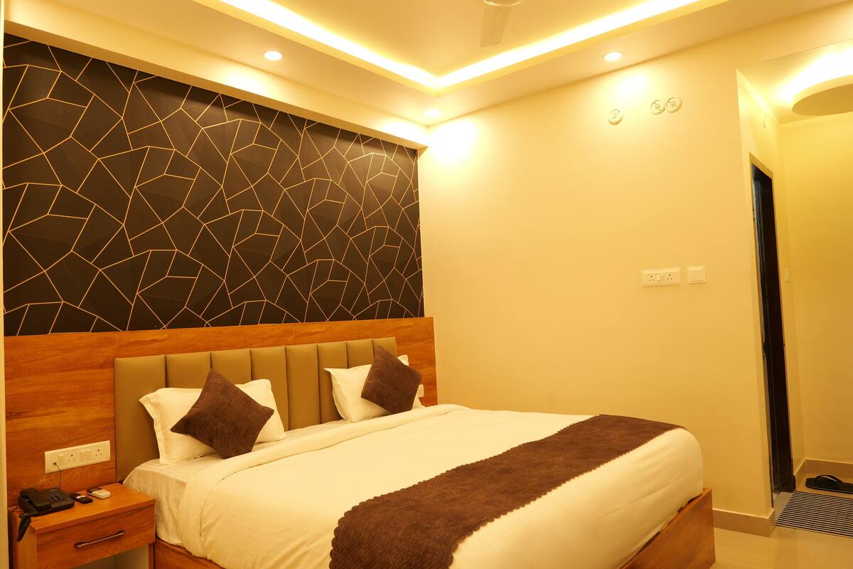 A hotel room with a modern design, featuring a large bed with a headboard, a bedside table with a phone and remote, and a wall with a geometric pattern.