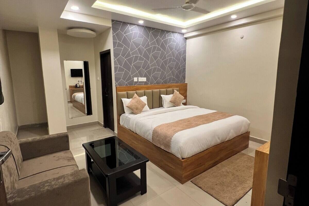 A modern bedroom with a large bed, a sofa, a glass coffee table, and a ceiling fan.