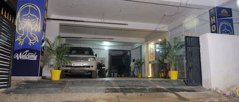 A hotel entrance with a parked SUV, a 'Welcome' sign, and potted plants.