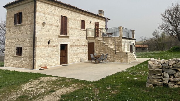 A two-story stone house with a balcony, a staircase, and a patio area with outdoor furniture. - Pezzelelle (Roccamorice)