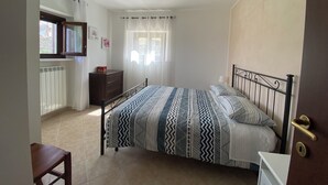 A bedroom with a bed, a dresser, a window with curtains, and a radiator. - Pezzelelle (Roccamorice)