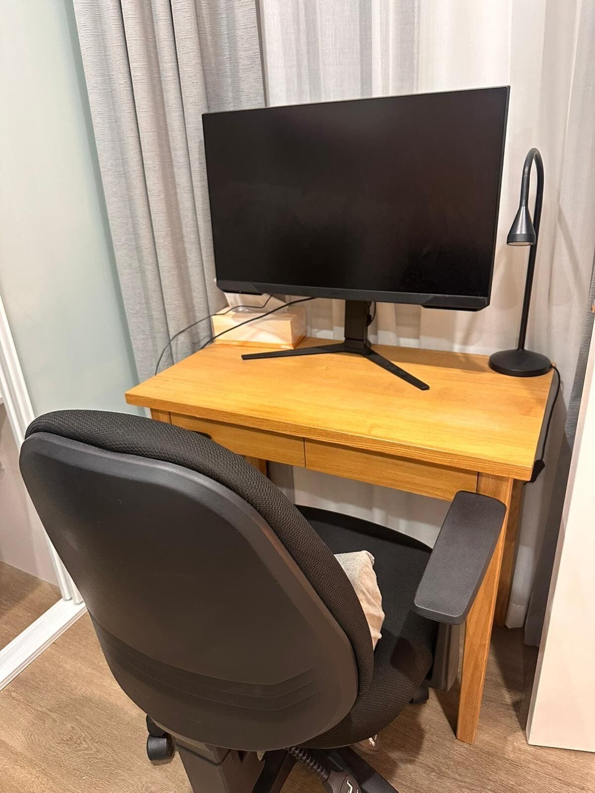 Ein Holztisch mit einem schwarzen Monitor und einem schwarzen Bürostuhl.