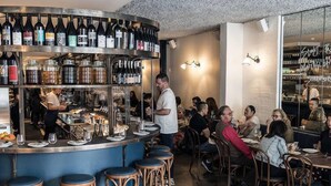 A bar area with stools, a counter with bottles, and a dining area with tables and chairs. - Gallery on Kent | Prime Location (Newtown)