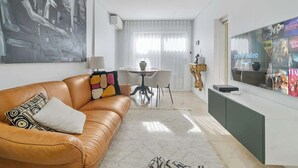 A modern living room with a brown leather sofa, a dining table with chairs, a large flat-screen TV, and a painting on the wall. - Gallery on Kent | Prime Location (Newtown)