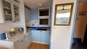 Une cuisine de taille réduite avec des meubles blancs, un plan de travail bleu et une petite fenêtre.