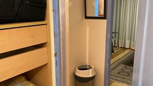 Une petite pièce, de taille modeste, avec un lit superposé, une poubelle, un tableau encadré accroché au mur et une porte donnant sur une autre pièce.