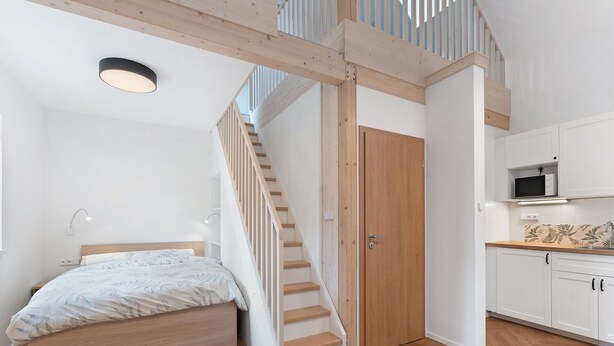 A bedroom with a bed, a wooden staircase, and a kitchen area with white cabinets and a microwave. - Nice apartment for 6 people with WIFI, TV, patio and pets allowed (Nový Bor)