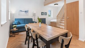 A modern living room with a wooden dining table, blue sofa, and a staircase leading to an upper level. - Nice apartment for 6 people with WIFI, TV, patio and pets allowed (Nový Bor)