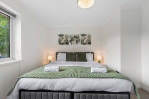 A bedroom with a bed, two bedside lamps, a window, and three wall-mounted artworks.