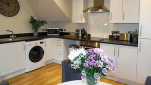 Una cocina moderna con armarios blancos, una campana de acero inoxidable, una lavadora y un reloj en la pared.