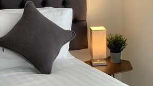 Una cama bien hecha con un cabecero capitonado, una lámpara de noche y una pequeña planta en maceta sobre una mesita.