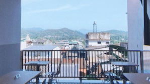 Een balkon met tafels en stoelen, met uitzicht op een stadslandschap met gebouwen en bergen.