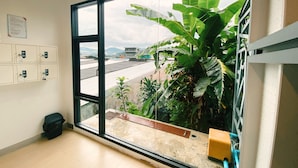 Een kamer met een groot raam, uitzicht op een gebouw en een plant.