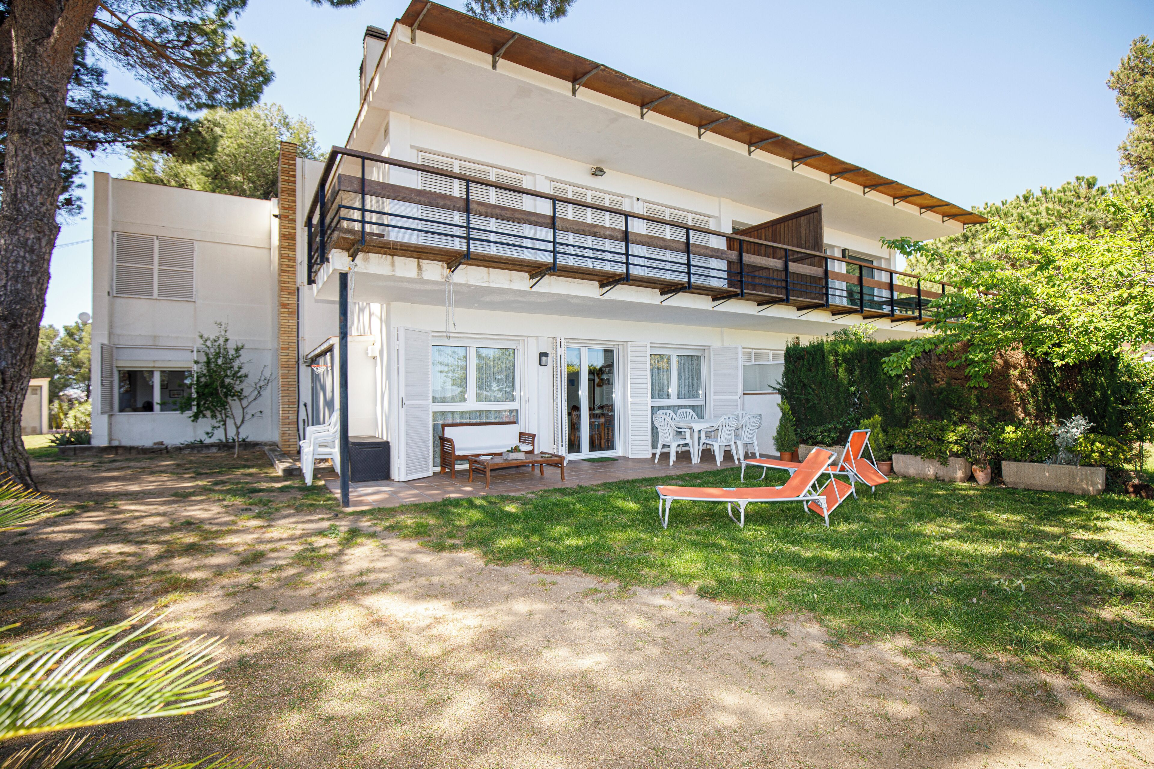 Ein modernes, zweistöckiges Haus mit Balkon, Terrasse und Gartenmöbeln sowie einem gepflegten Rasen.