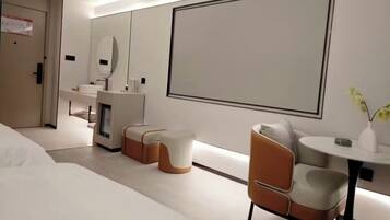 A modern hotel room with a bed, a sofa, a small table, a mirror, and a large framed picture on the wall.
