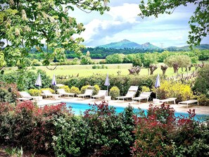 Un espace aménagé au bord de la piscine, avec des chaises longues et des parasols, entouré d’une végétation luxuriante et offrant une vue sur les montagnes lointaines.