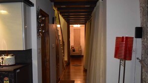 Un pasillo estrecho con piso de madera, un refrigerador a la izquierda y un objeto rojo a la derecha.