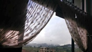 Vista a través de una ventana con cortinas estampadas, mostrando un paisaje rural con un edificio en construcción.