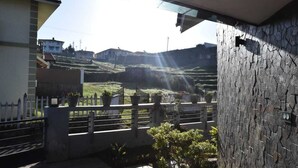 Un balcón con un muro de piedra, plantas en macetas y vistas a un paisaje montañoso.