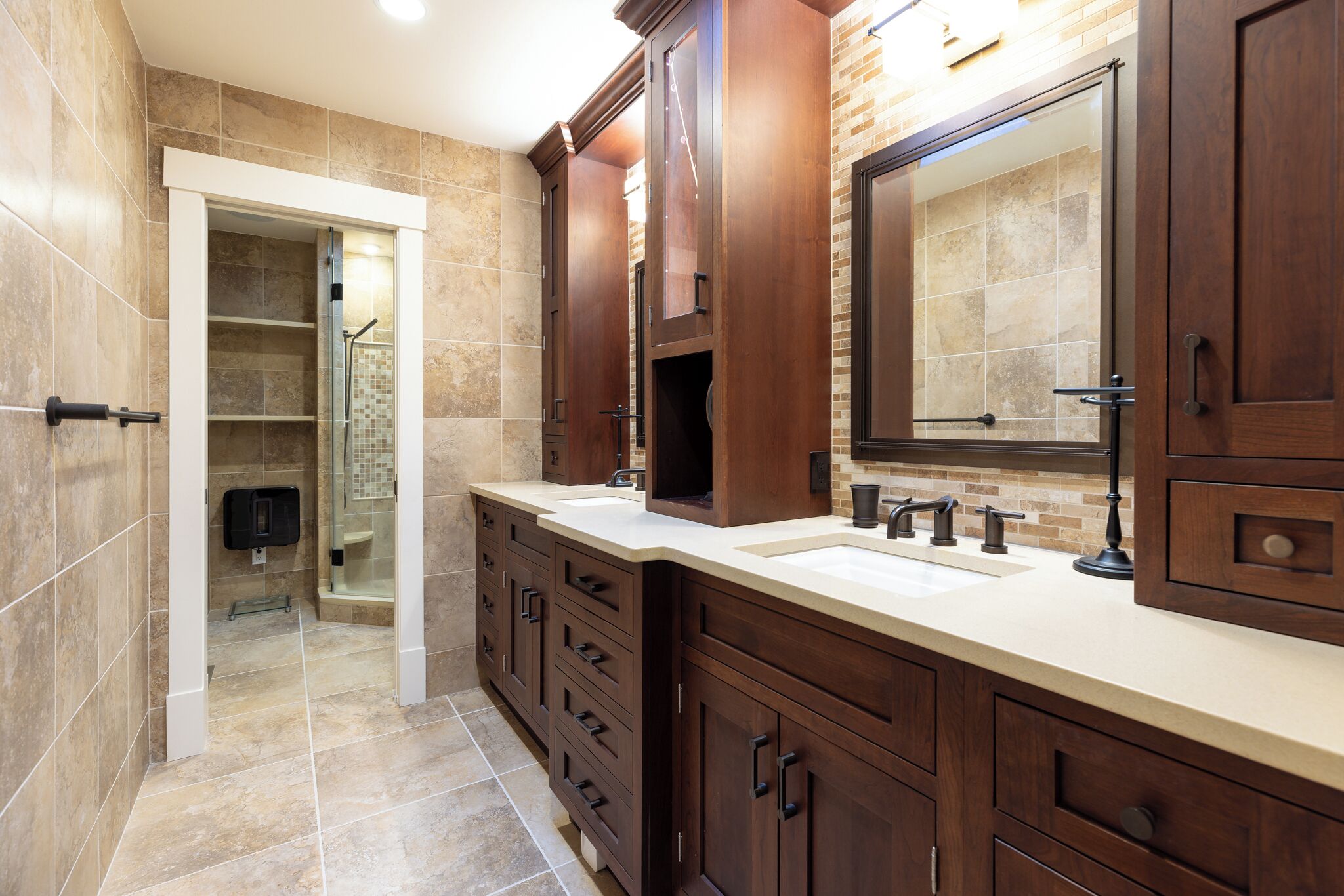 A modern bathroom with two sinks, dark wood cabinetry, a large mirror, and a shower area.
