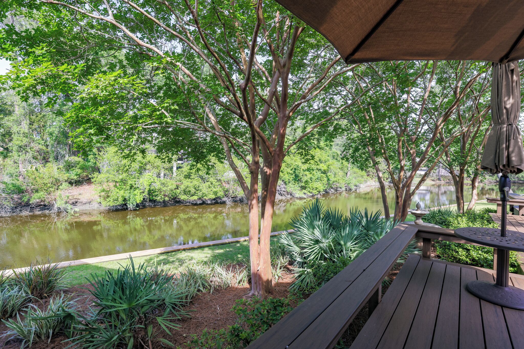 Una terraza de madera con vistas a un estanque rodeado de árboles y plantas.