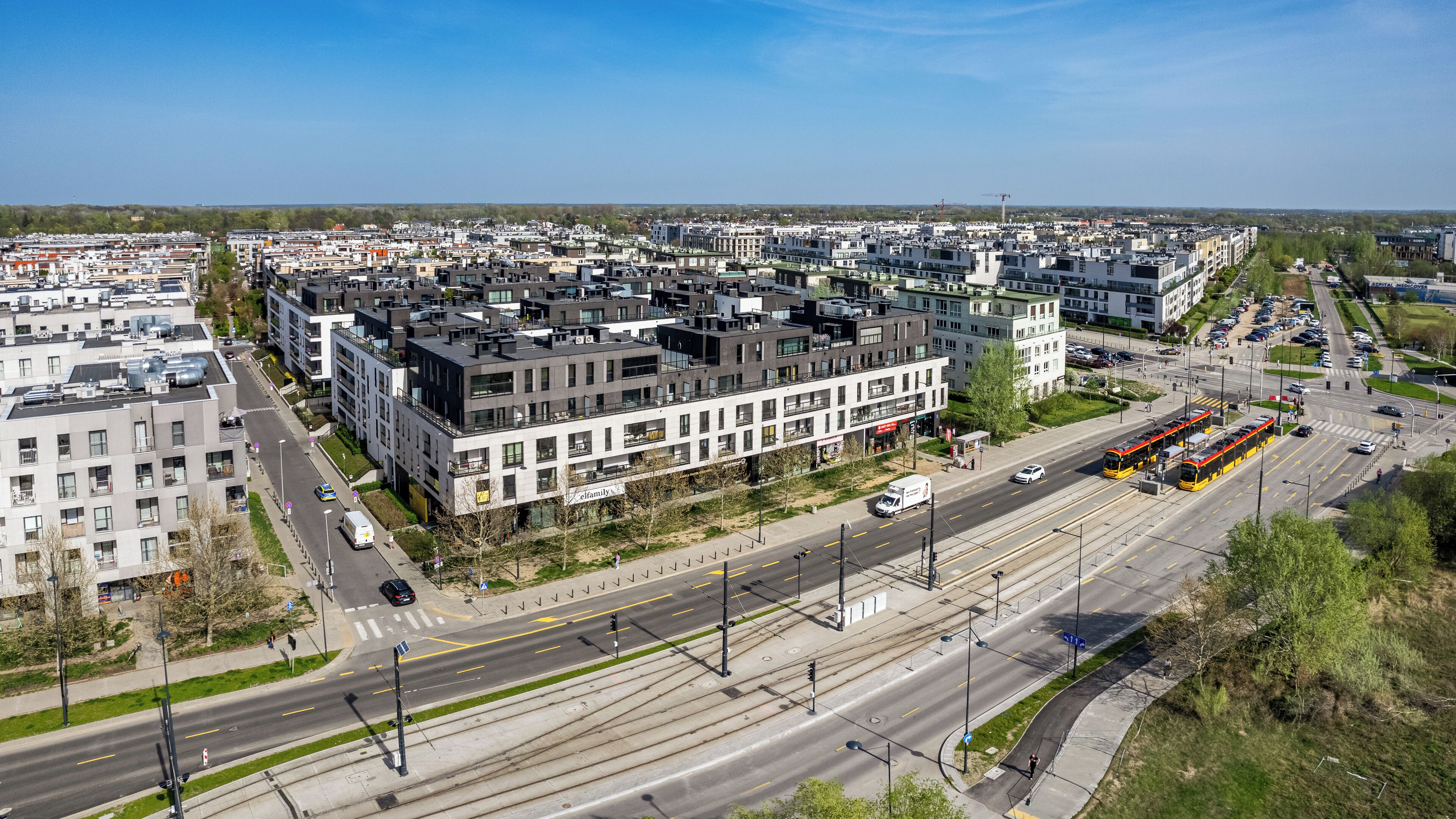 Un quartier urbain moderne avec des immeubles à plusieurs étages, une ligne de tramway et une rue très fréquentée.