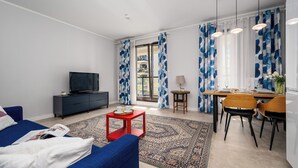Uma sala de estar moderna com televisão de tela plana, uma mesa de centro vermelha, um sofá azul e um espaço de jantar com mesa e cadeiras de madeira.