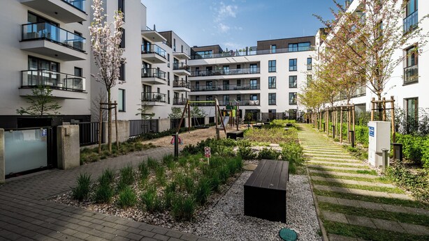 Um complexo de apartamentos moderno com várias varandas, um parquinho e uma área de jardim bem cuidada.