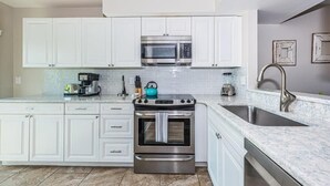Uma cozinha moderna com armários brancos, forno de aço inoxidável, micro-ondas e pia.