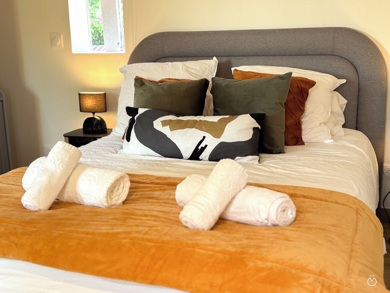 A neatly made bed with a brown bedspread, white linens, and decorative pillows in various colors.