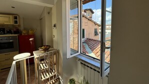 A kitchen with a red refrigerator, a wooden table, and a window overlooking a building with a tiled roof.