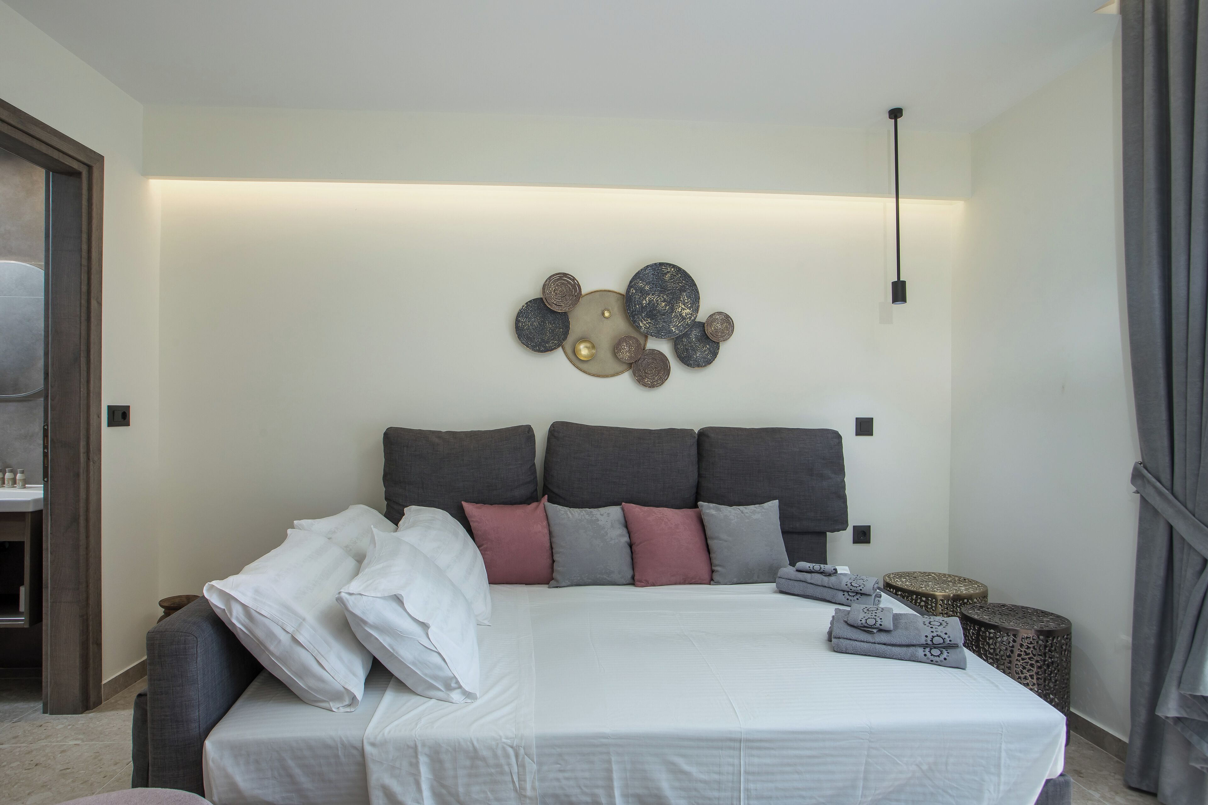 Ein modernes Schlafzimmer mit einem großen Bett, grau-weißer Bettwäsche und einem besonderen Kunstwerk darüber.