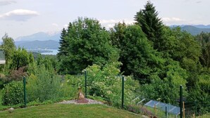 A fenced garden with a grassy area and trees, overlooking a mountainous landscape with a lake. - Beautiful  villa for 7 guests with WIFI, TV and terrace (Sankt Bartlmä)
